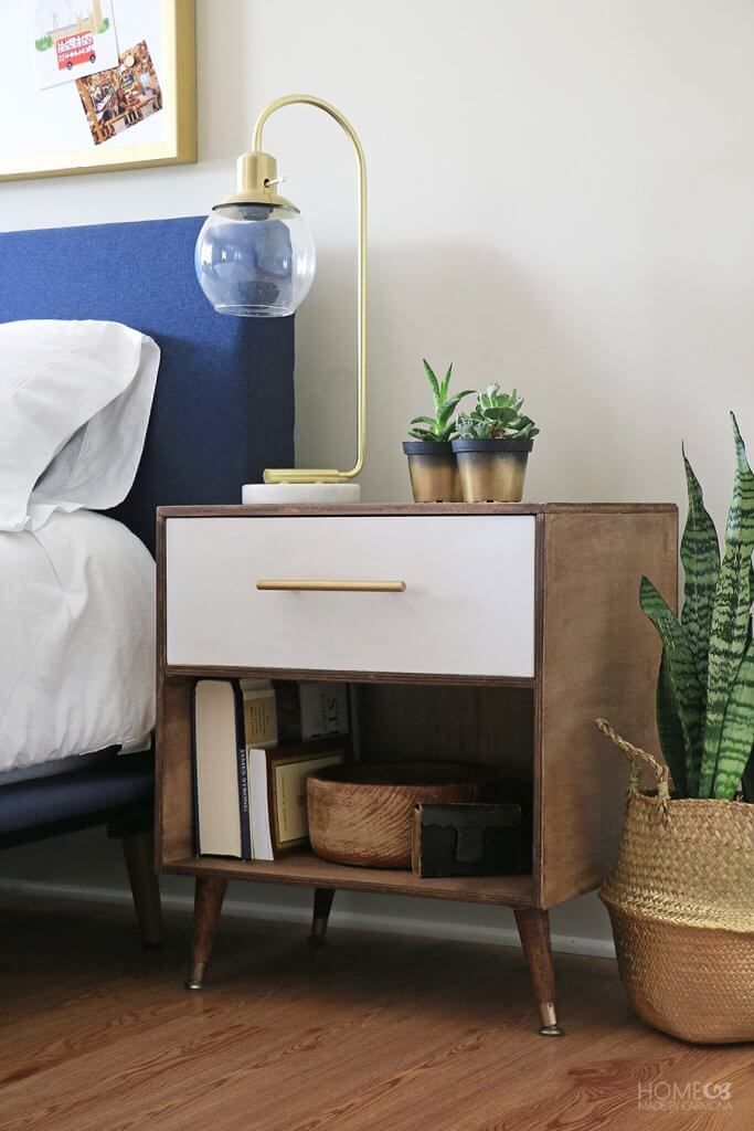 a bed with a blue headboard and a white nightstand next to a potted plant