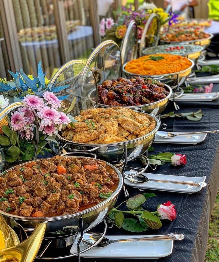 a long table with many different types of food on it and flowers in the background