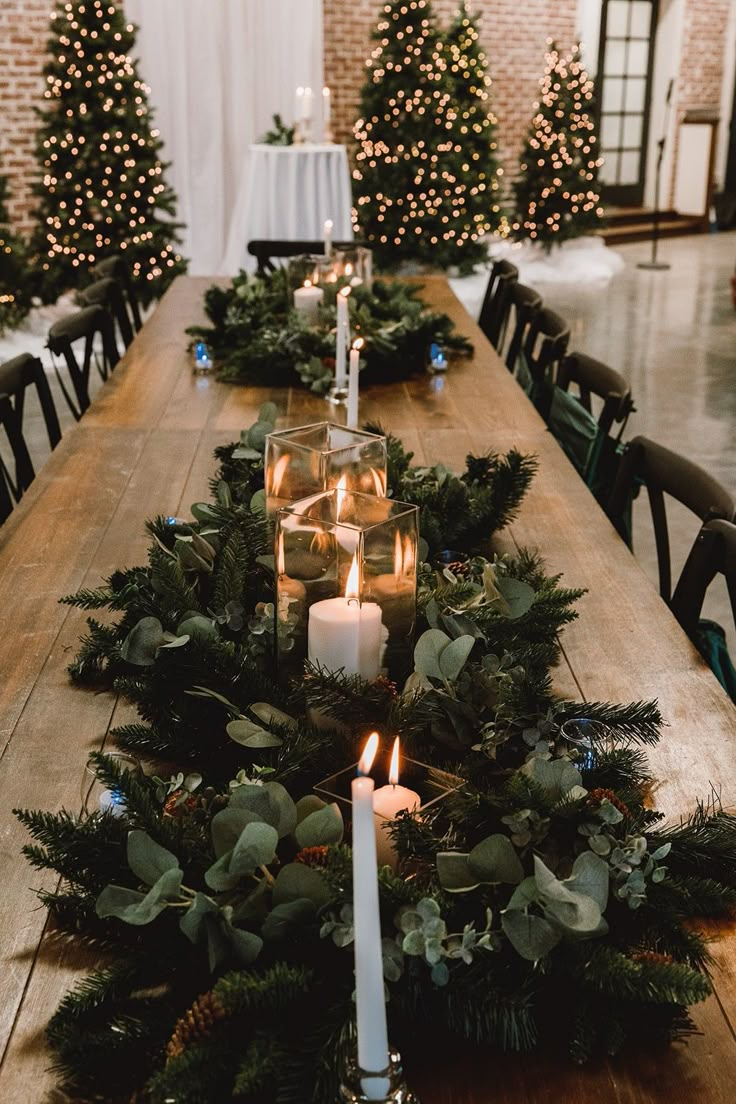 a long wooden table with candles and greenery on the top, surrounded by christmas trees