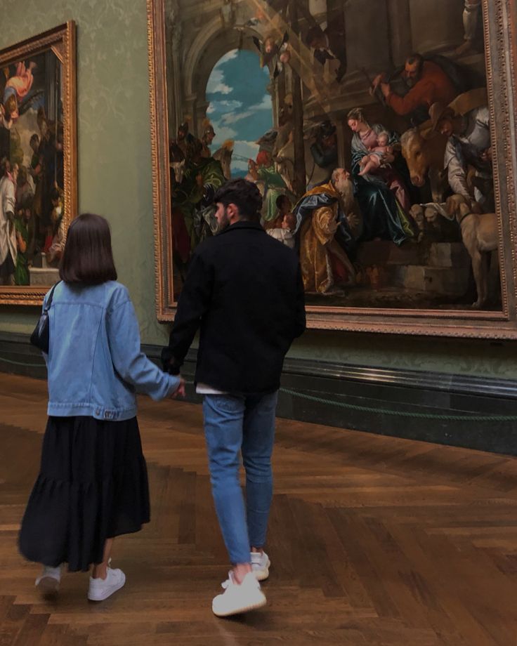 two people holding hands in front of paintings