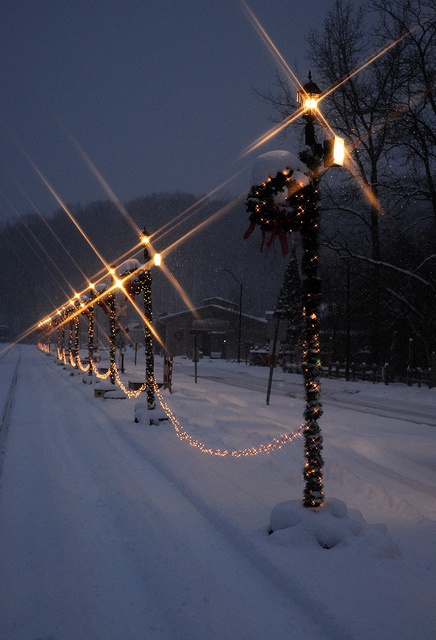 a row of lights that are on the side of a road in the snow at night