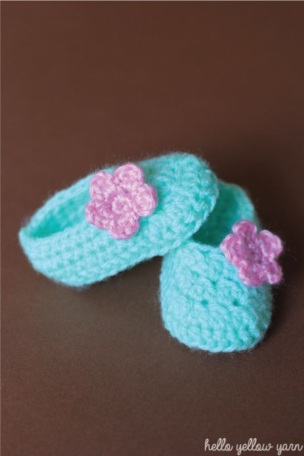 two crocheted blue slippers with pink flowers on them sitting on a brown surface