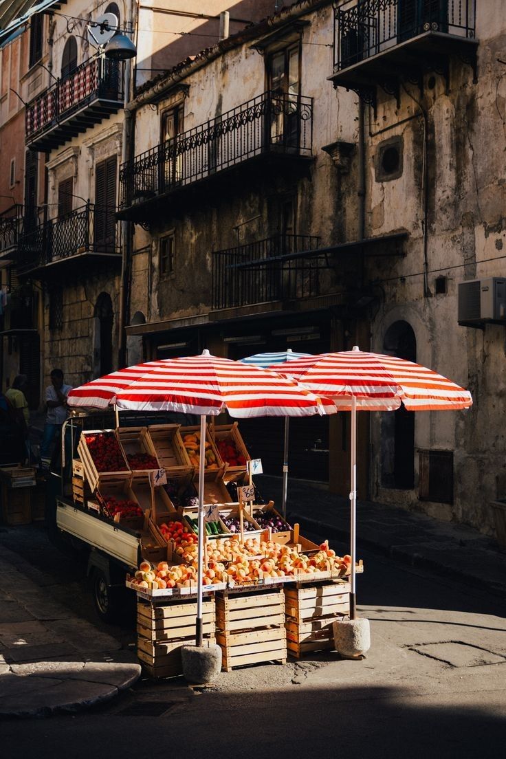 an open air fruit and vegetable stand on the side of a road in front of buildings