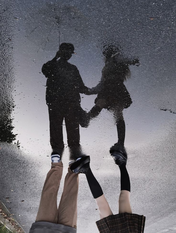 two people standing in the rain holding hands and looking at each other with their reflection