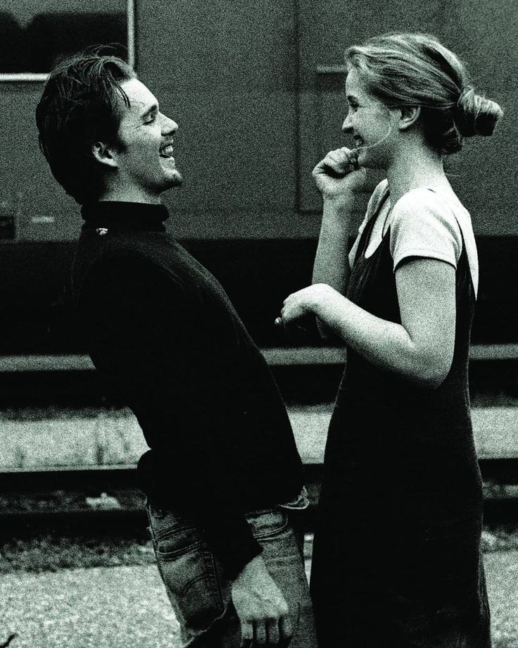 a man and woman standing next to each other on the side of a train track