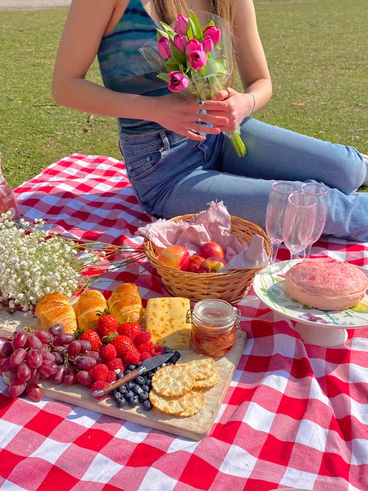 a woman sitting on a picnic blanket with food and wine in front of her,