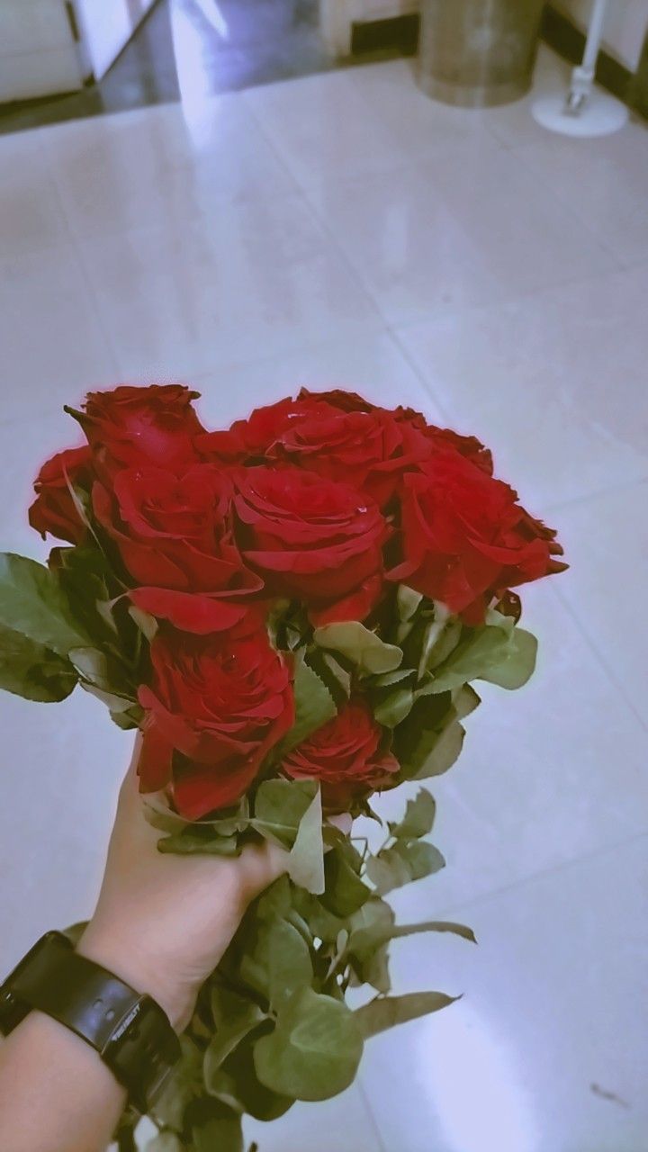 a person holding a bunch of red roses in their hand on the floor next to a tile floor