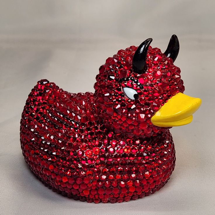 a red sequinized rubber duck sitting on top of a white surface with a yellow beak