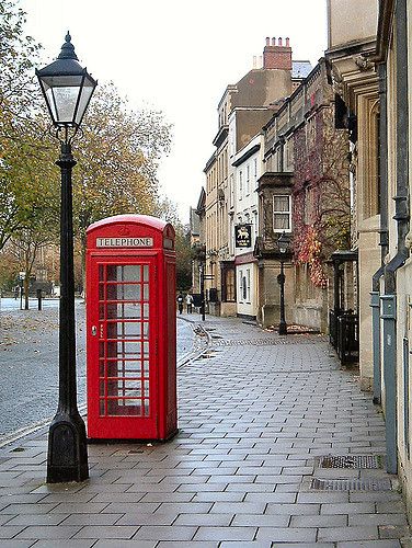 a red phone booth sitting on the side of a street next to a lamp post