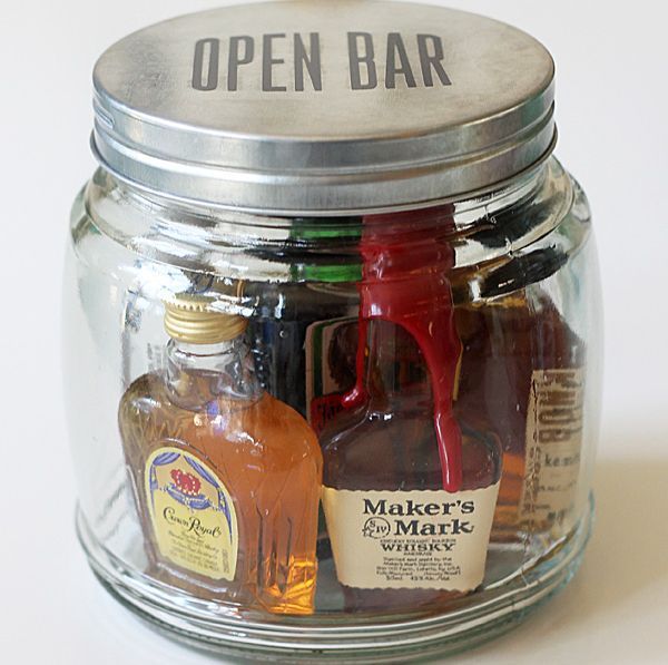 a glass jar filled with liquor bottles on top of a white table next to an open bar sign