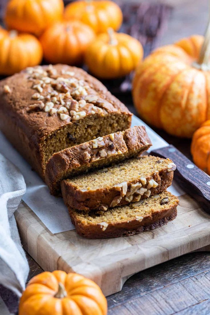 sliced loaf of pumpkin bread sitting on top of a cutting board next to mini pumpkins