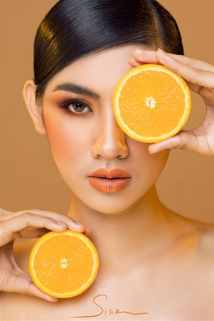 a woman holding two orange slices in front of her face