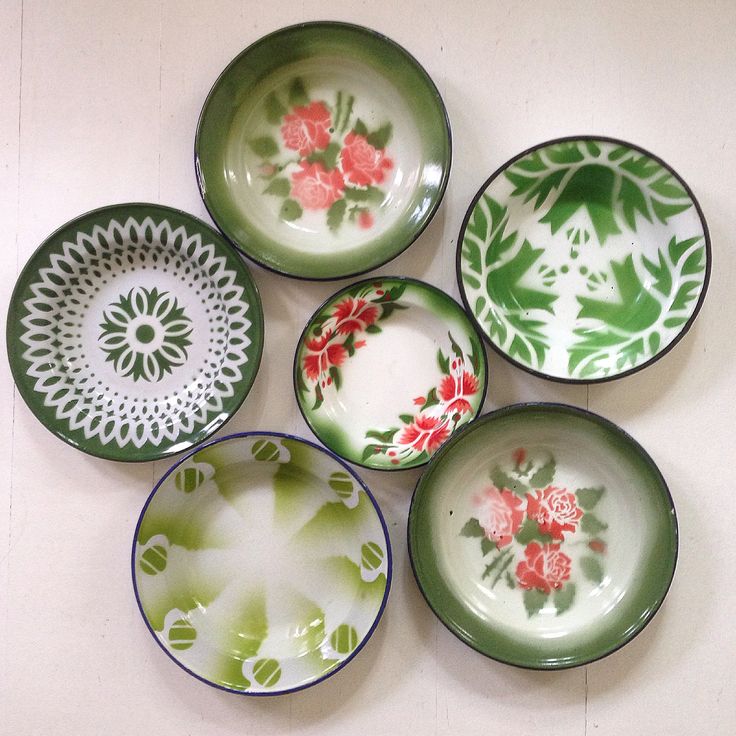 four plates with flowers painted on them are arranged in a row, one is green and the other is pink