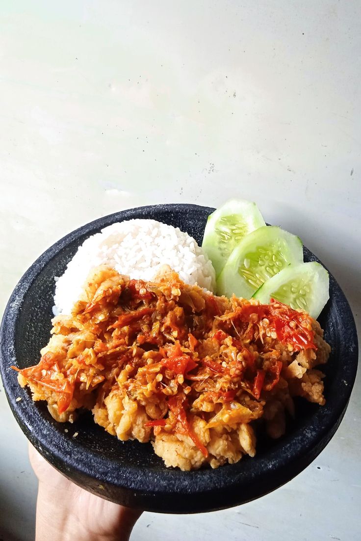 a person holding a plate with rice, meat and vegetables