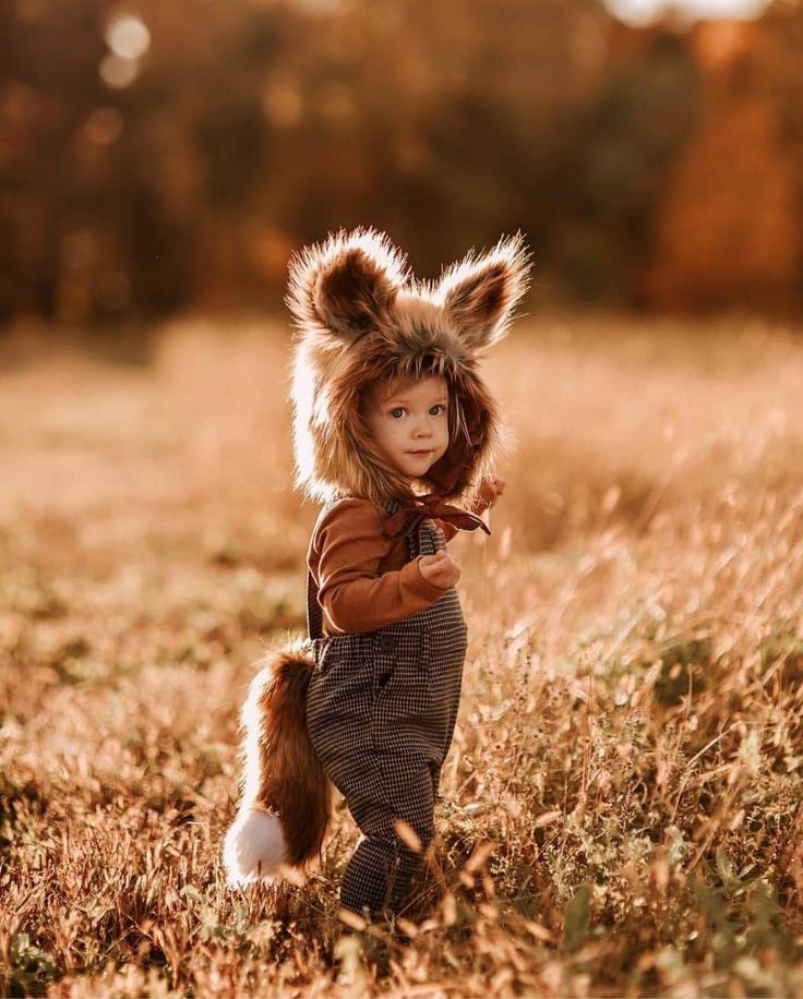 a small child wearing a furry animal hat and overalls is walking through the grass