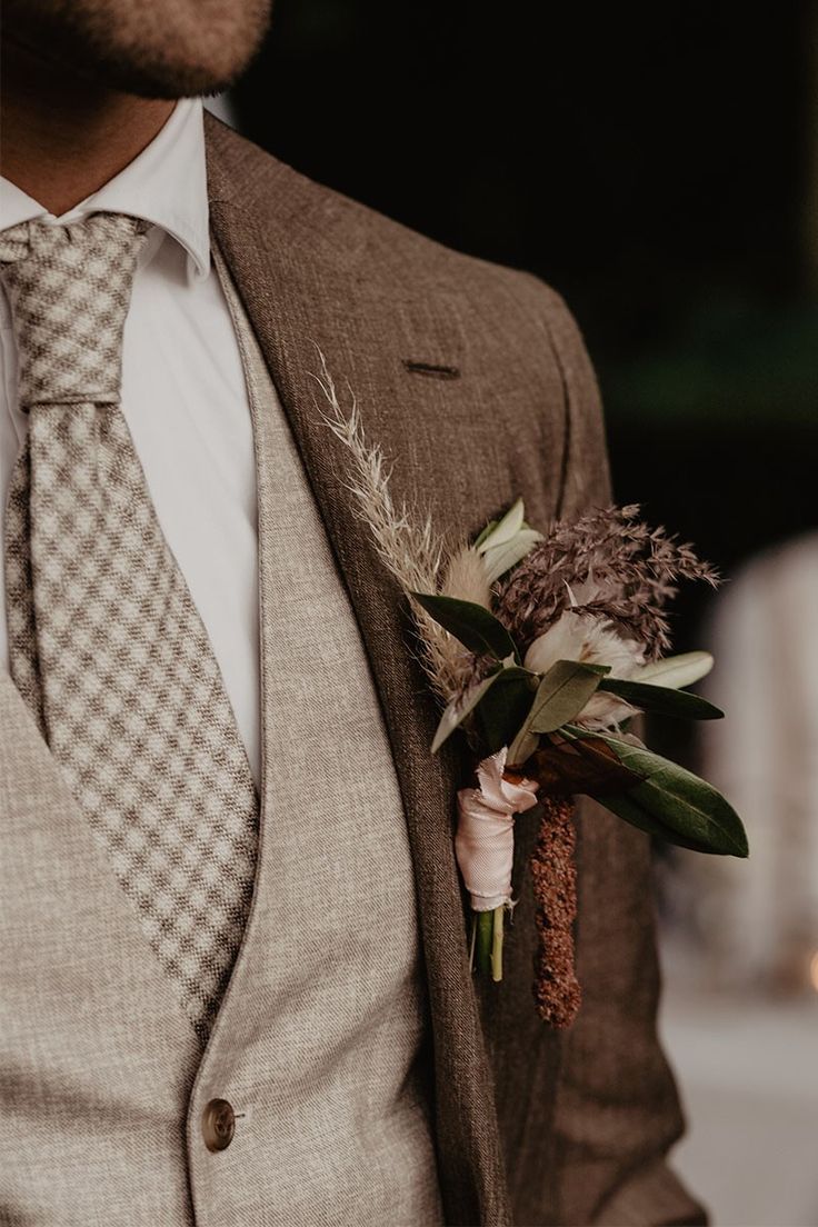 a close up of a person wearing a suit and tie holding a boutonniere