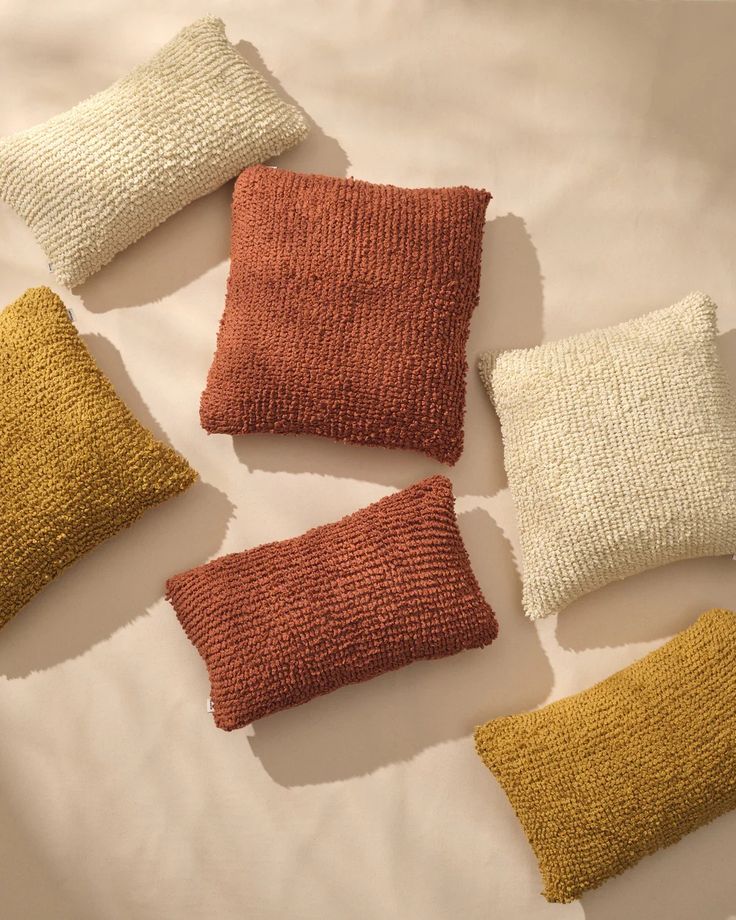 four different colored pillows sitting on top of a white bed spread with one orange and the other yellow