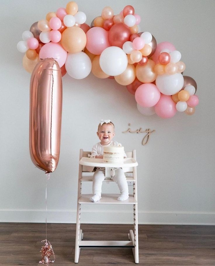 a baby sitting in a chair next to a bunch of balloons and a balloon arch