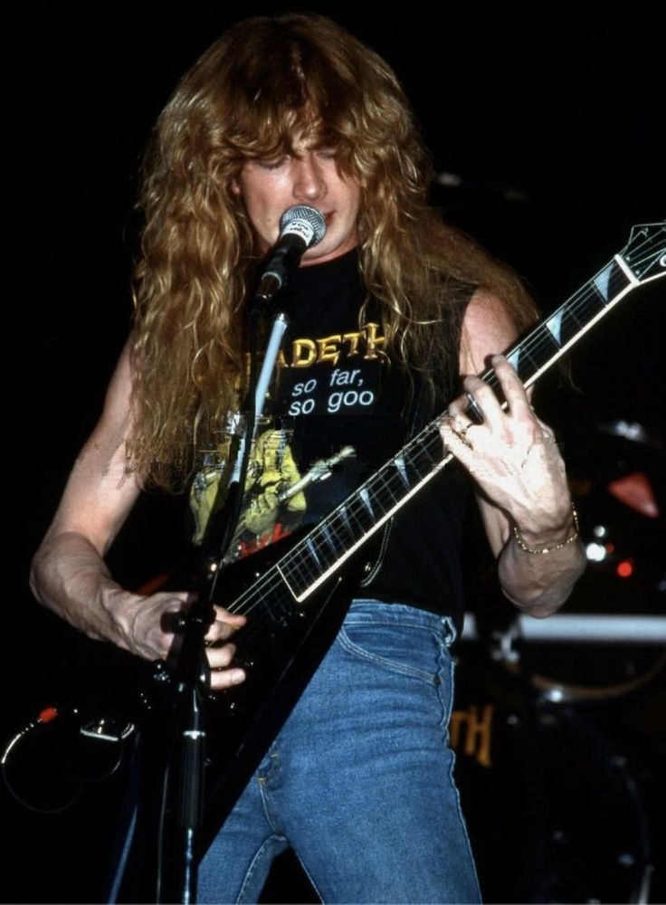 a man with long hair holding a guitar and singing into a microphone at a concert