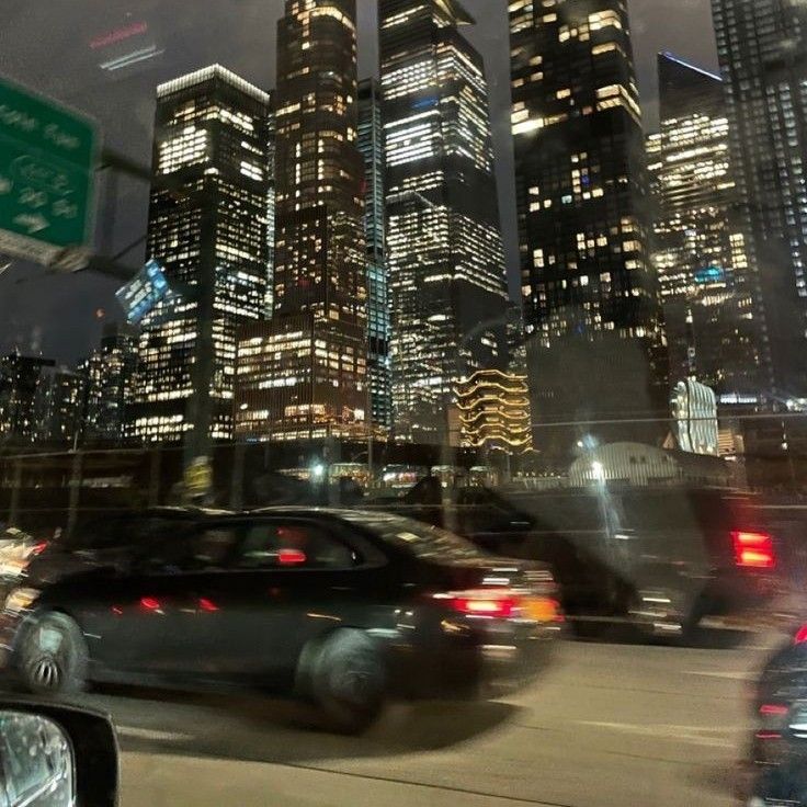 the city skyline is lit up at night as cars drive down the street in front of them