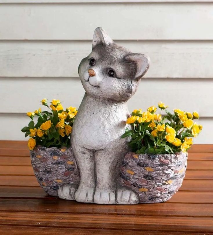 a statue of a cat sitting on top of a wooden table next to yellow flowers