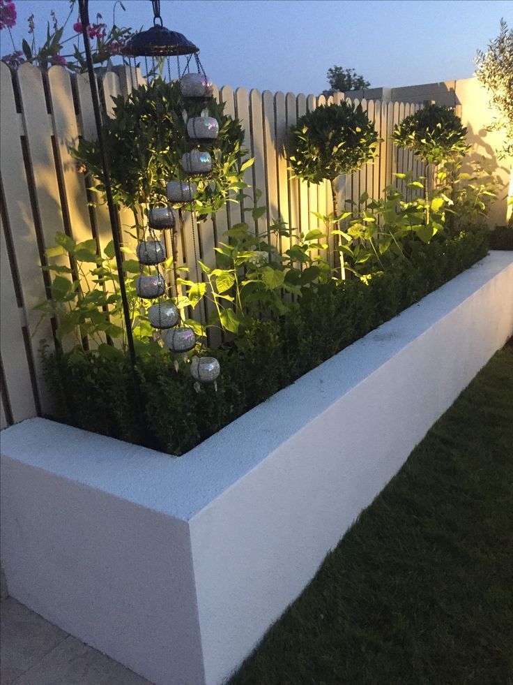 a white planter filled with lots of plants next to a fence and grass area