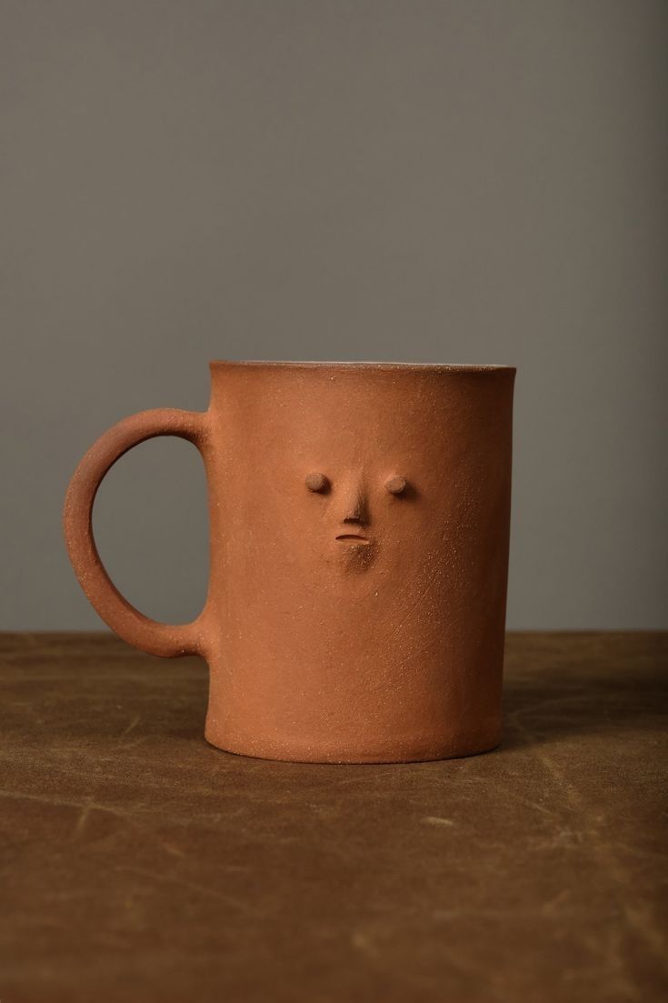 a clay mug with a face drawn on the outside of it, sitting on a table