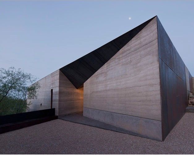 an unusual building with a triangular roof sits in the middle of a desert landscape at dusk