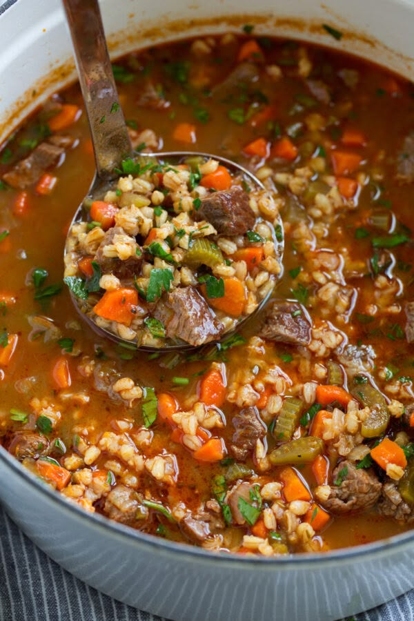 a ladle full of soup with meat, vegetables and rice in it on top of a table