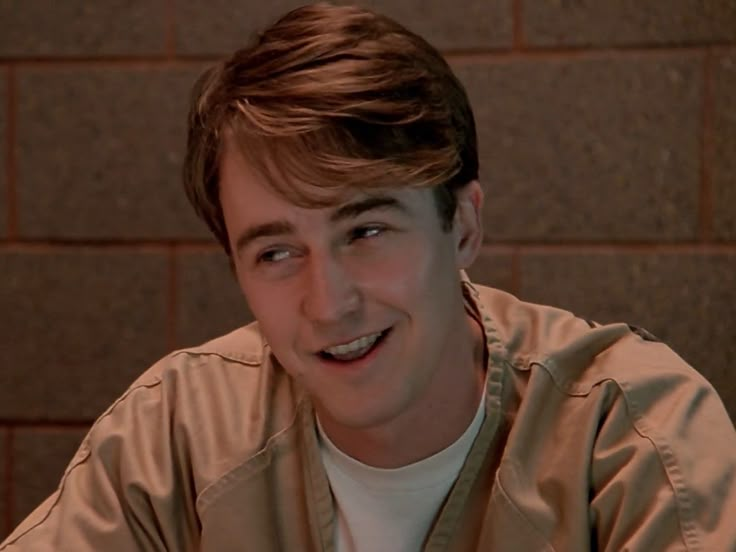 a young man is smiling in front of a brick wall