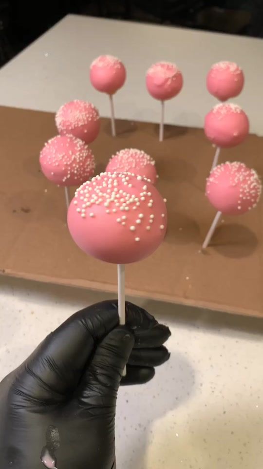 a person in black glove holding up pink cake pops