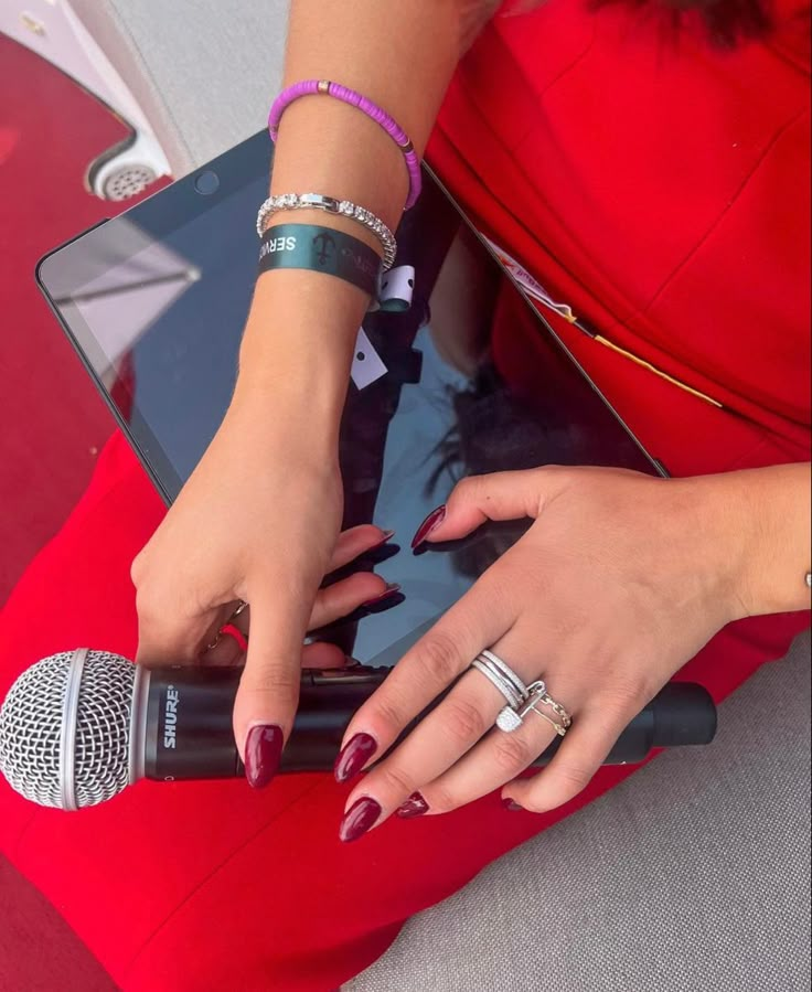 a woman in a red dress is holding a microphone and looking at her cell phone