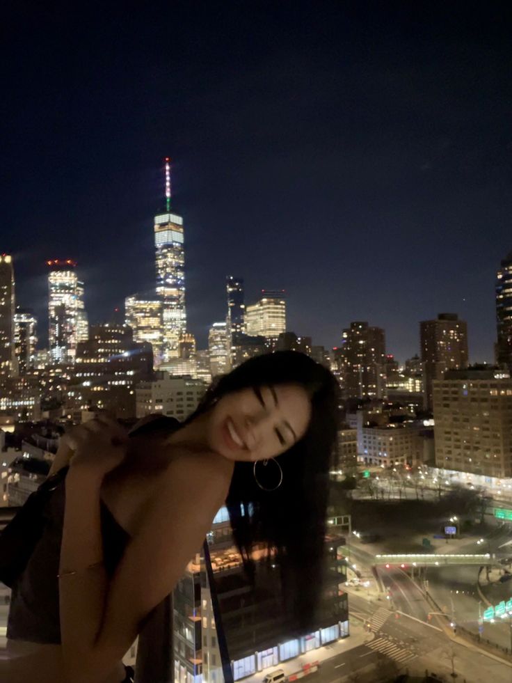 a woman standing on top of a building in front of a cityscape at night