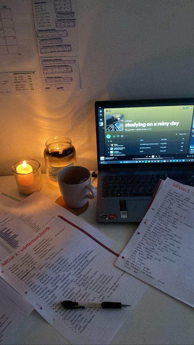 an open laptop computer sitting on top of a desk next to papers and a candle