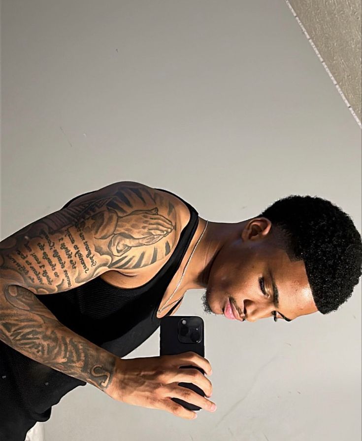 a man with tattoos taking a selfie in front of a mirror while holding a cell phone