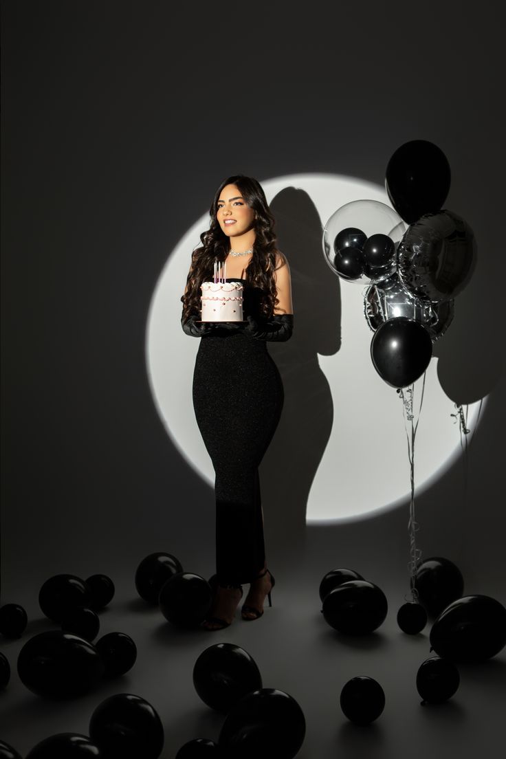 a woman holding a cake standing in front of balloons