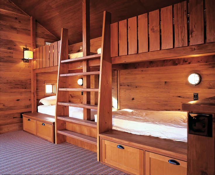 a bunk bed in a room with wooden walls and drawers on the bottom floor, next to a ladder