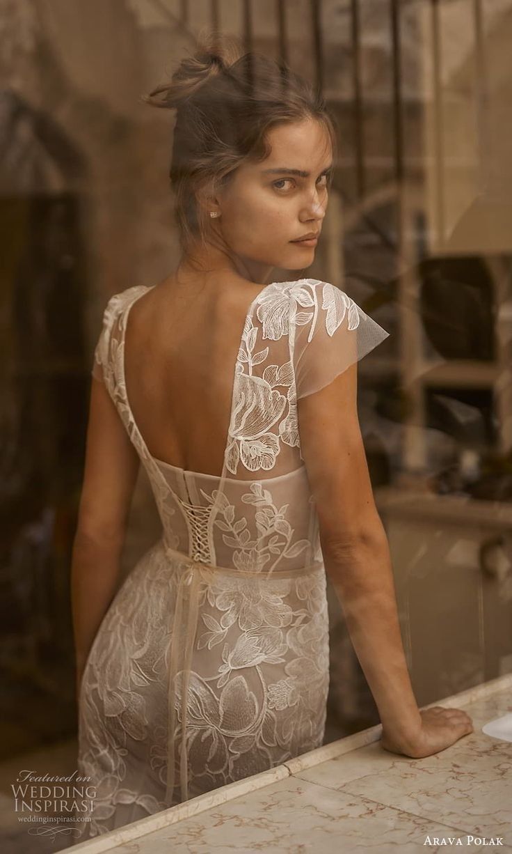 a woman standing in front of a window with her back turned to the camera and wearing a white dress