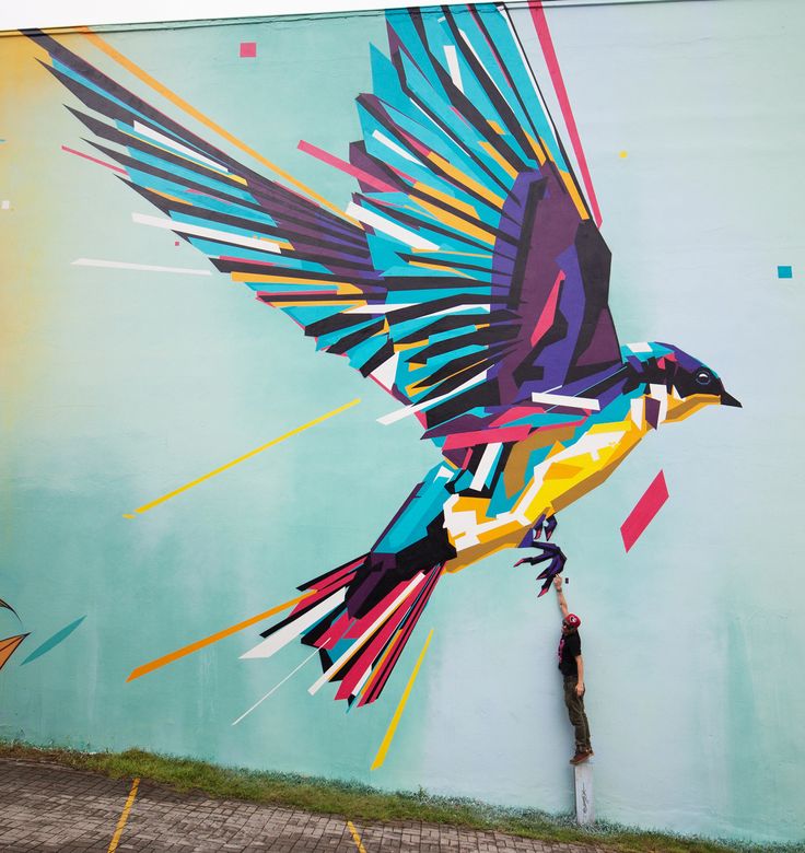 a man standing in front of a colorful bird painted on the side of a building