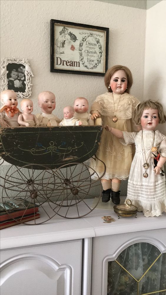 a group of dolls standing on top of a white cabinet next to a baby carriage