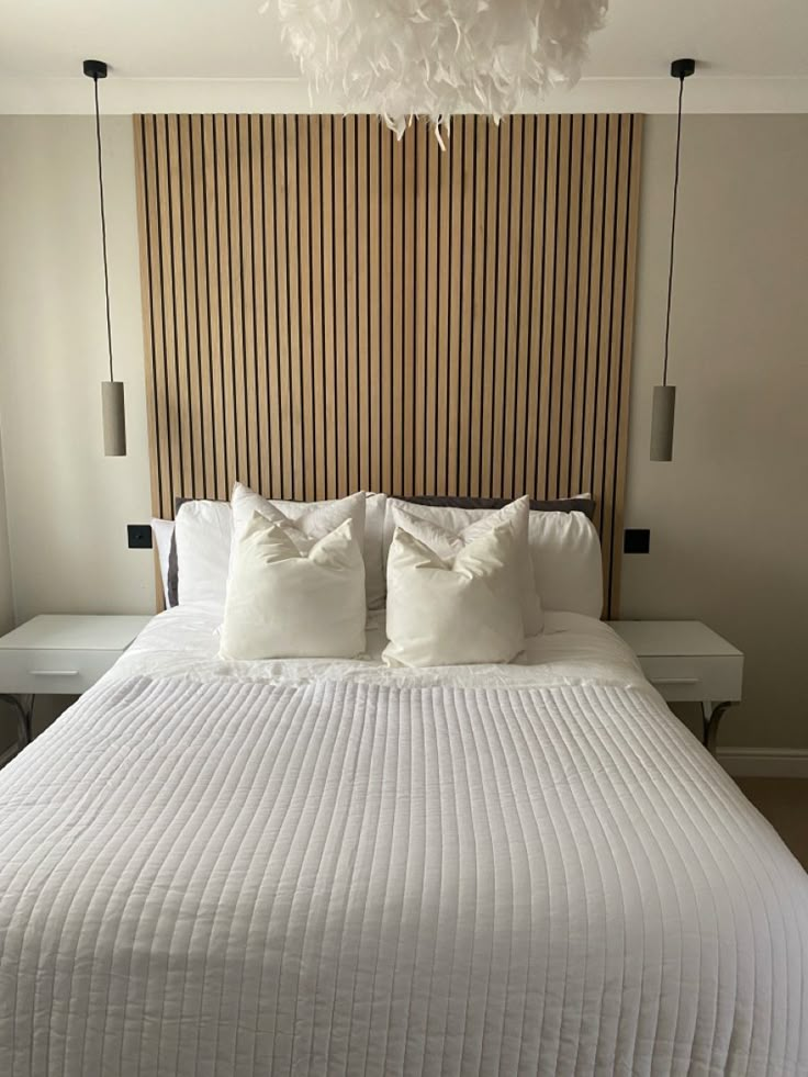 a white bed with two pillows on it and a headboard made out of wood slats