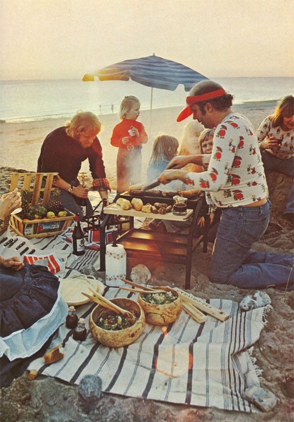 a group of people sitting on top of a beach next to the ocean eating food