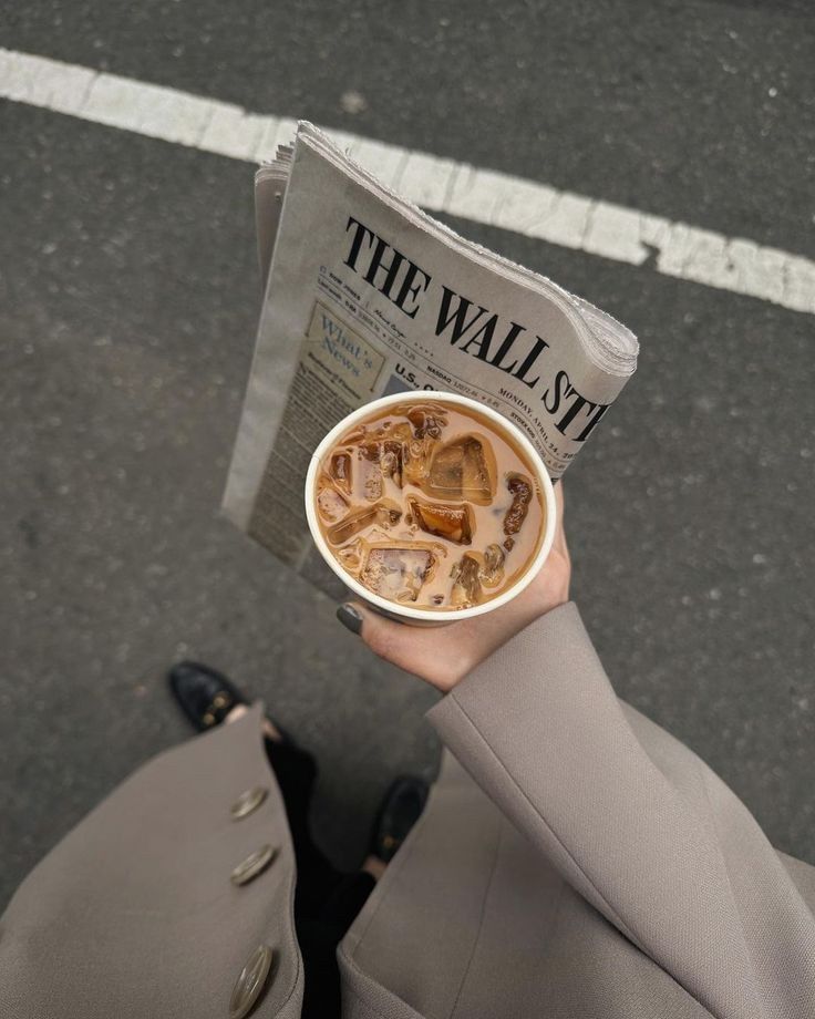 a person holding up a newspaper and a cup of coffee