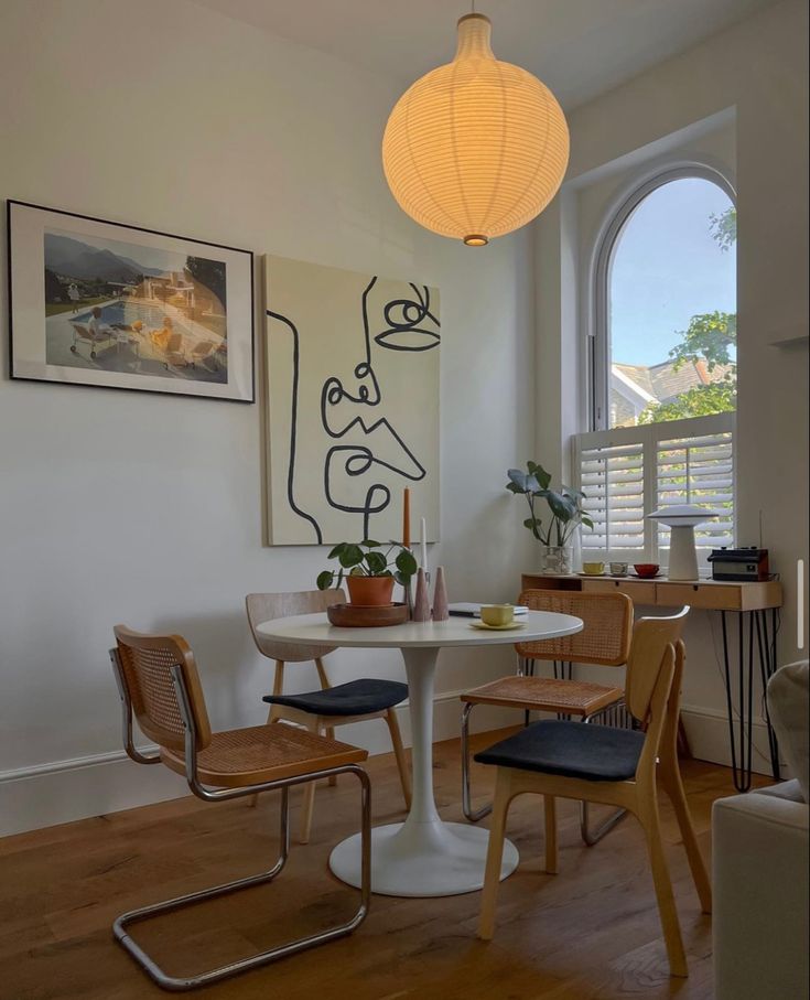 a dining room table and chairs in front of a large window with an art work on the wall