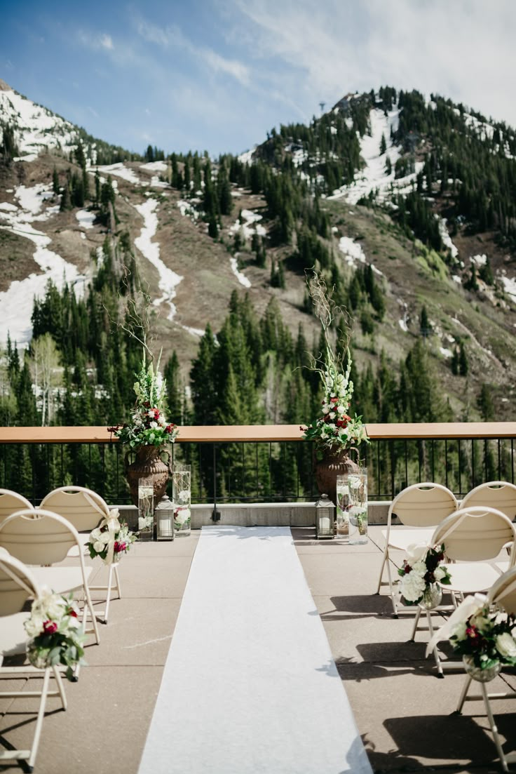 an outdoor ceremony set up with white chairs and flowers on the aisle in front of snowy mountains