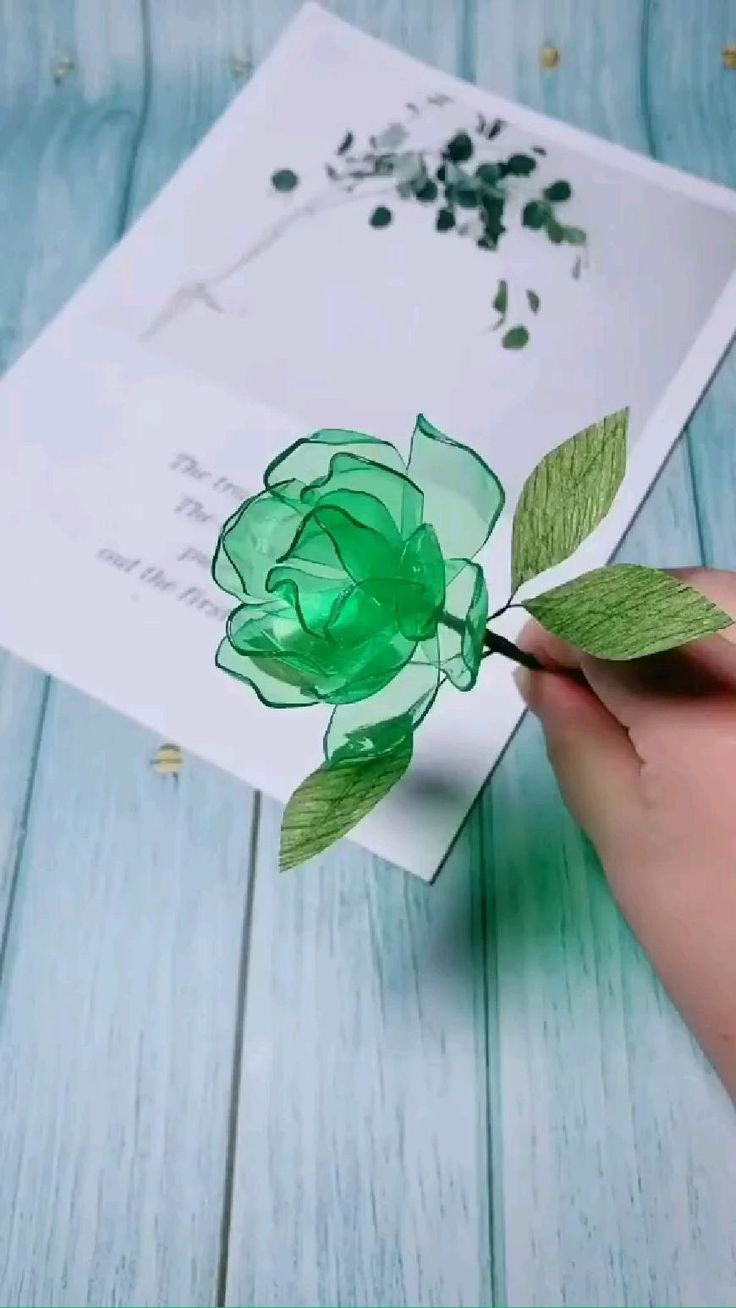 someone is holding a green flower in front of a piece of paper with leaves on it