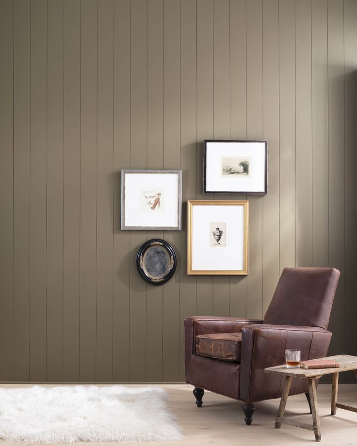 a brown chair sitting next to a wooden table in front of a wall with pictures on it