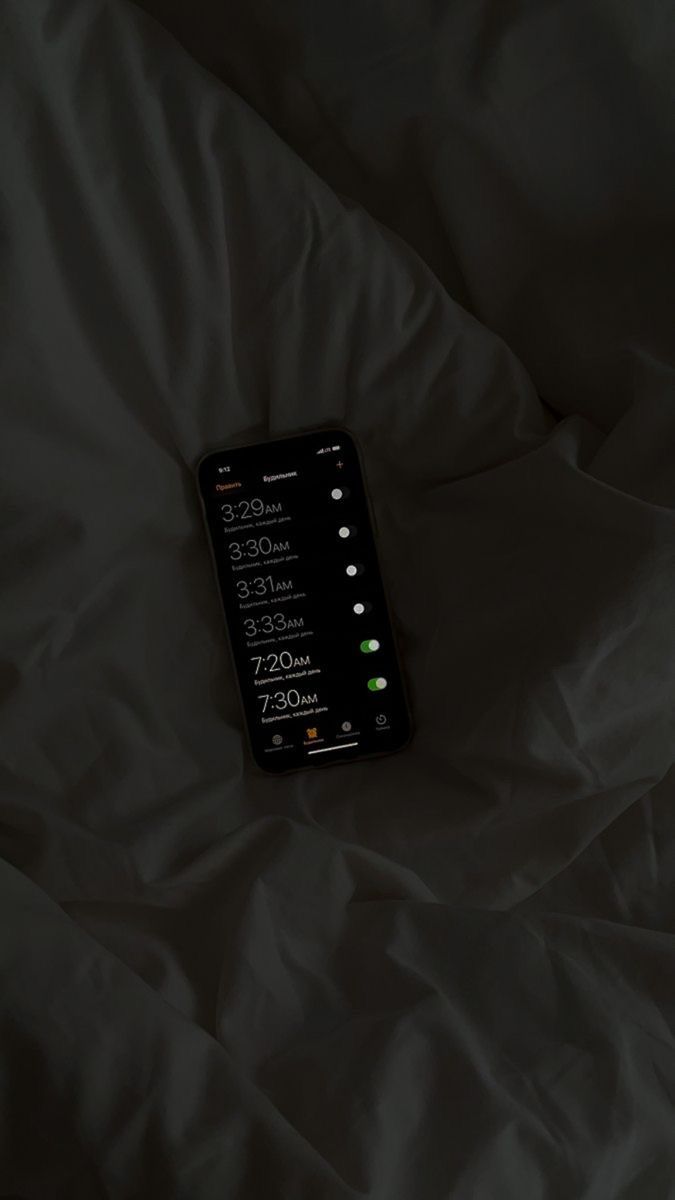 a cell phone sitting on top of a bed covered in white sheets with the time displayed