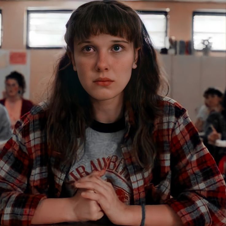 a young woman sitting at a table with her hands folded in front of her chest