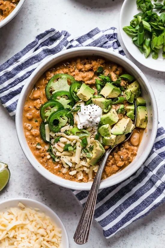 two bowls filled with chili, beans and avocado on top of a table